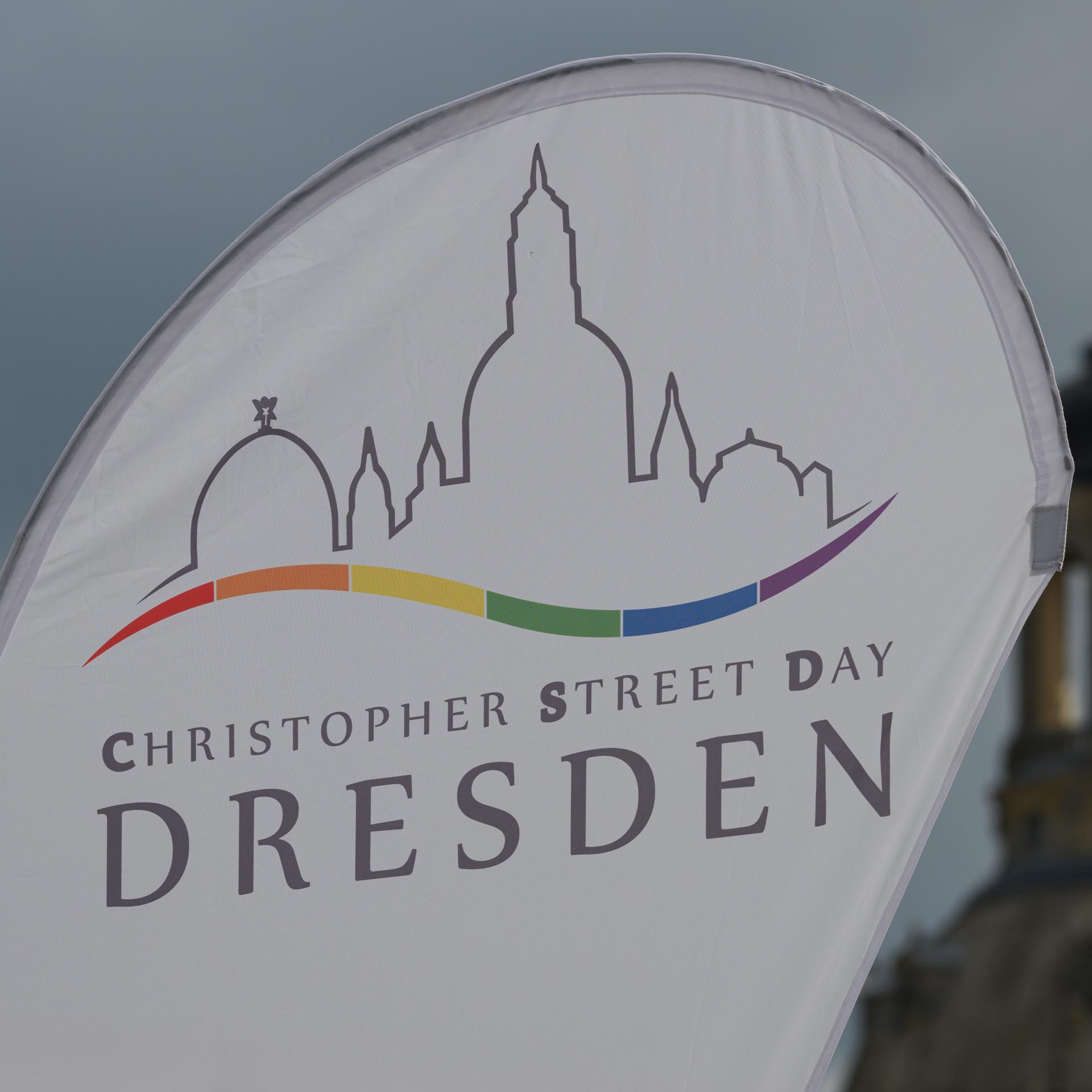 Eine Fahne mit dem Logo und der Aufschrift "Christopher Street Day Dresden" weht auf dem Altmarkt der sächsischen Stadt im Wind.