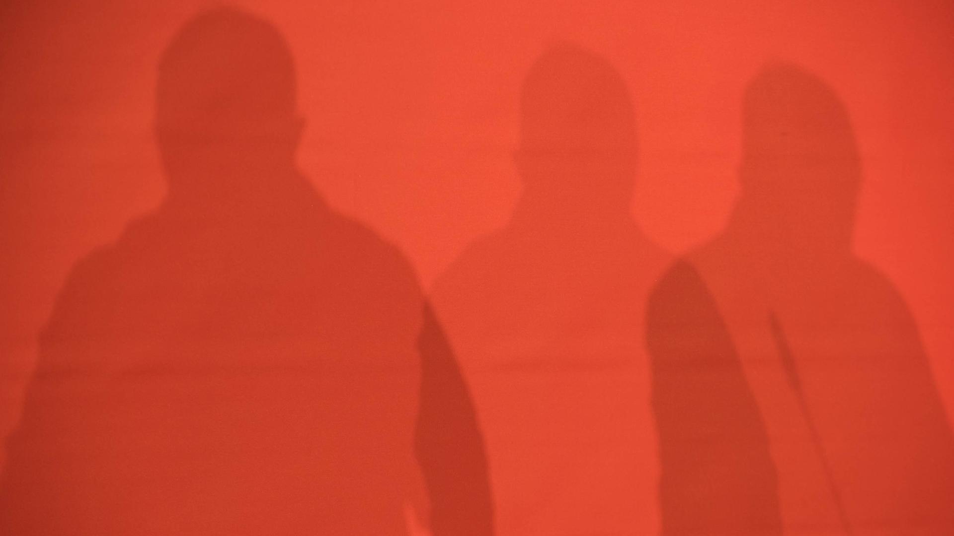 Schatten von drei Personen auf einer roten Wand. Landesparteitag der Partei Die Linke in Berlin.