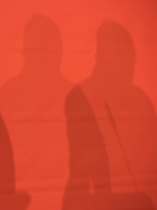 Schatten von drei Personen auf einer roten Wand. Landesparteitag der Partei Die Linke in Berlin.