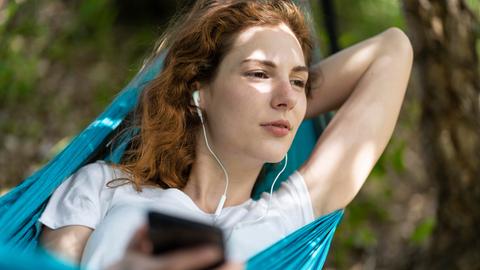 Eine Frau entspannt in einer Hängematte und trägt Kopfhörer.
