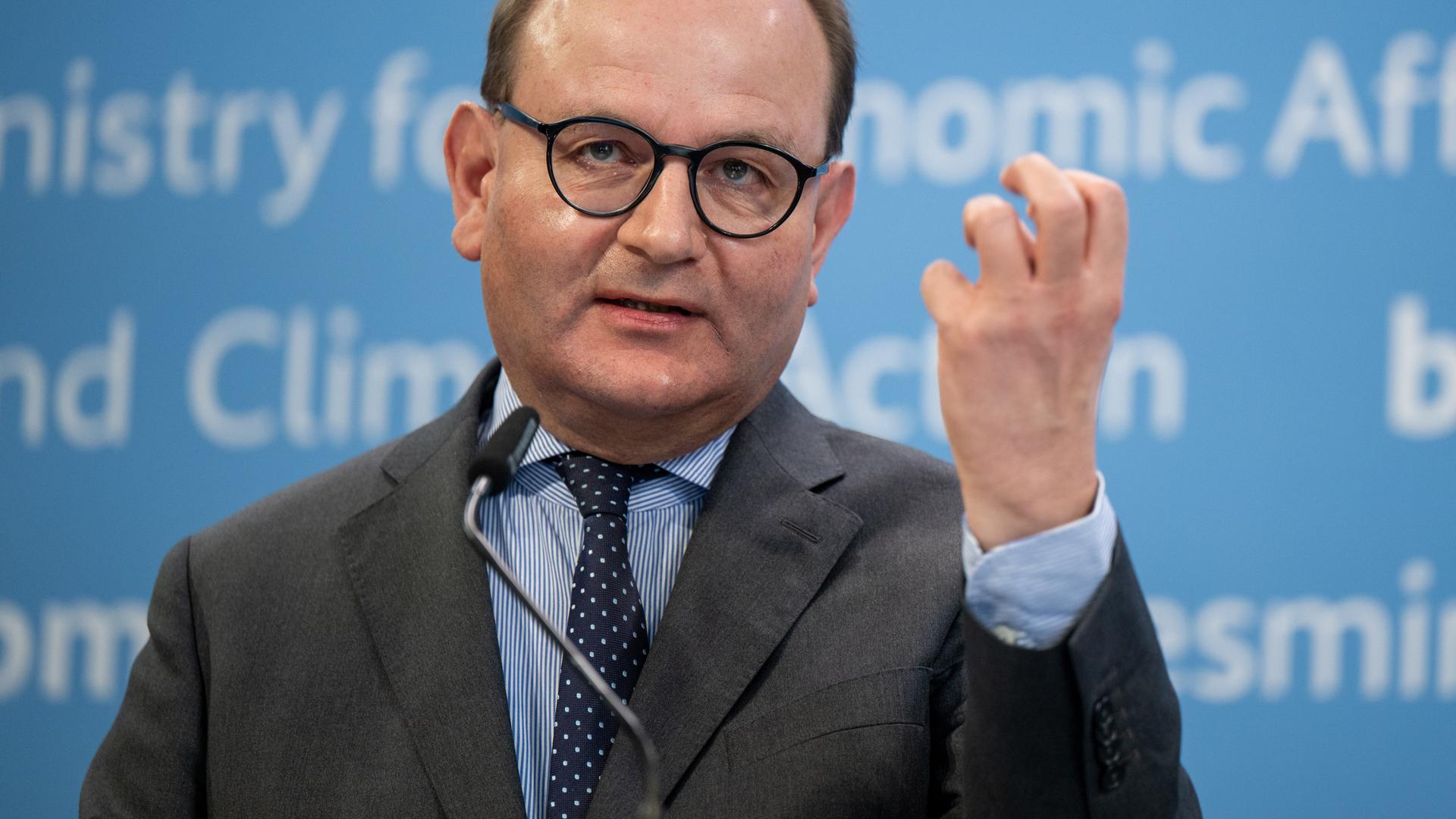 Ottmar Edenhofer spricht gestikulierend vor einer blauen Wand