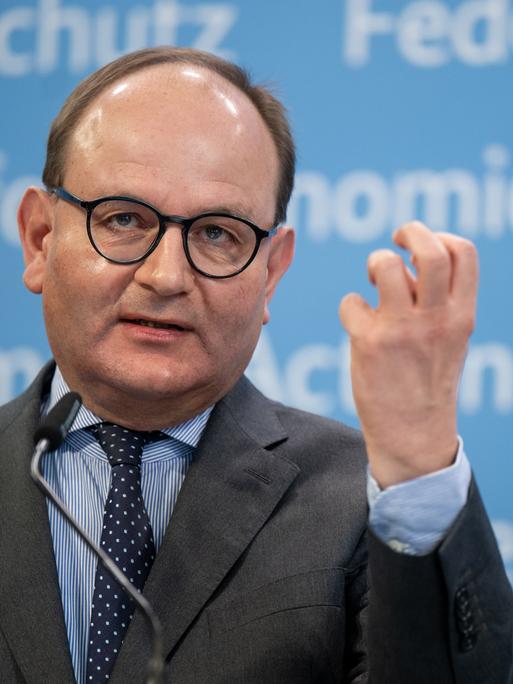 Ottmar Edenhofer spricht gestikulierend vor einer blauen Wand