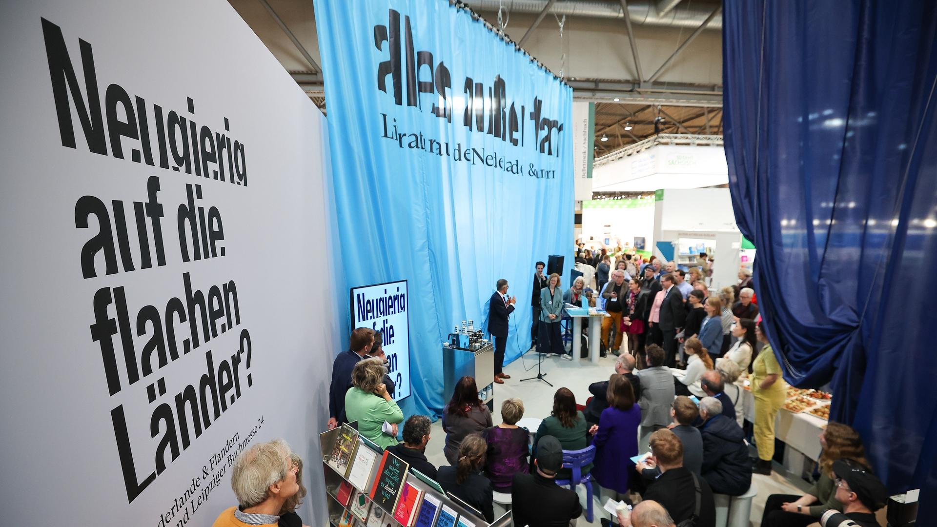 Messebesucher stehen am Stand der Niederlande, dem Gastland 2024, auf der Leipziger Buchmesse. Auf Planen ist zu lesen "Neugierig auf die flachen Länder?" 