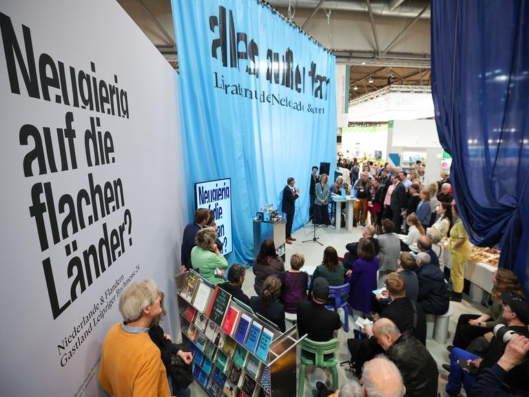 Messebesucher stehen am Stand der Niederlande, dem Gastland 2024, auf der Leipziger Buchmesse. Auf Planen ist zu lesen "Neugierig auf die flachen Länder?" 
