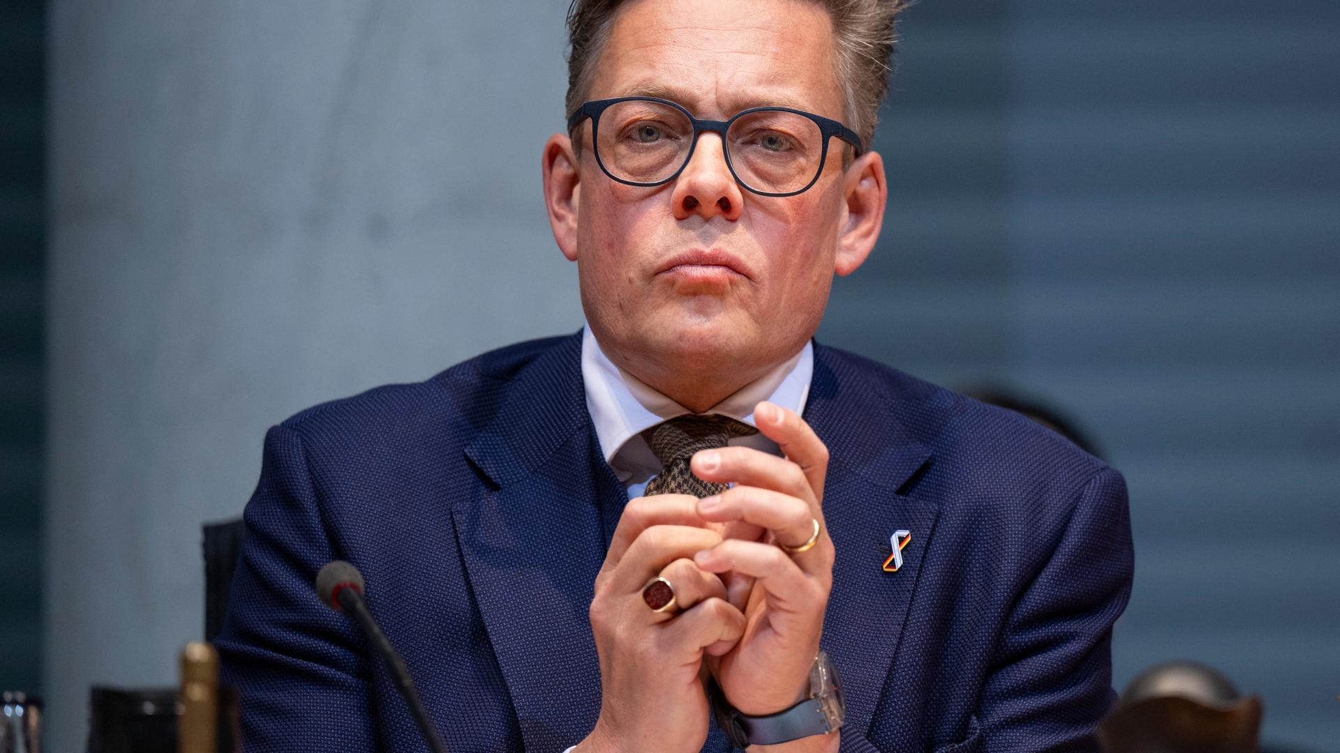 Konstantin von Notz (Bündnis 90/Die Grünen), Vorsitzender des Parlamentarischen Kontrollgremiums, blickt mit gespitztem Mund und gefalteten Händen in die Kamera. Er trägt ein blaues Sakko und Krawatte.