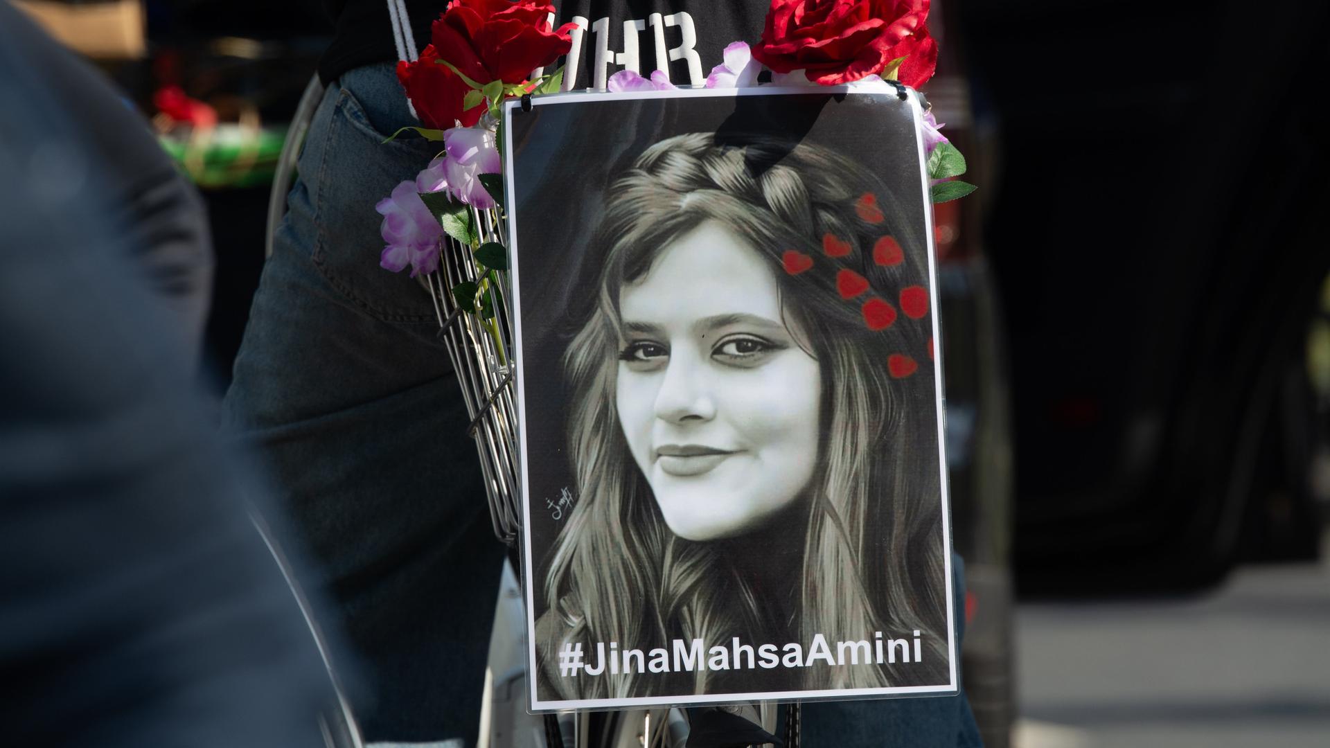 Ein schwarzweißes Porträt von Jina Mahsa Amini ist während einer Demonstration am Gepäckträger eines Fahrrads befestigt.