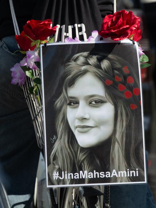 Ein schwarzweißes Porträt von Jina Mahsa Amini ist während einer Demonstration am Gepäckträger eines Fahrrads befestigt.