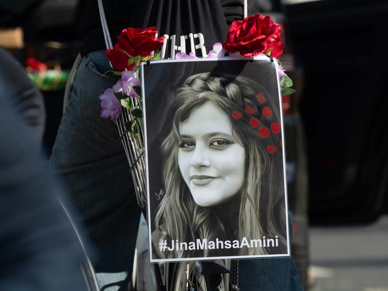 Ein schwarzweißes Porträt von Jina Mahsa Amini ist während einer Demonstration am Gepäckträger eines Fahrrads befestigt.