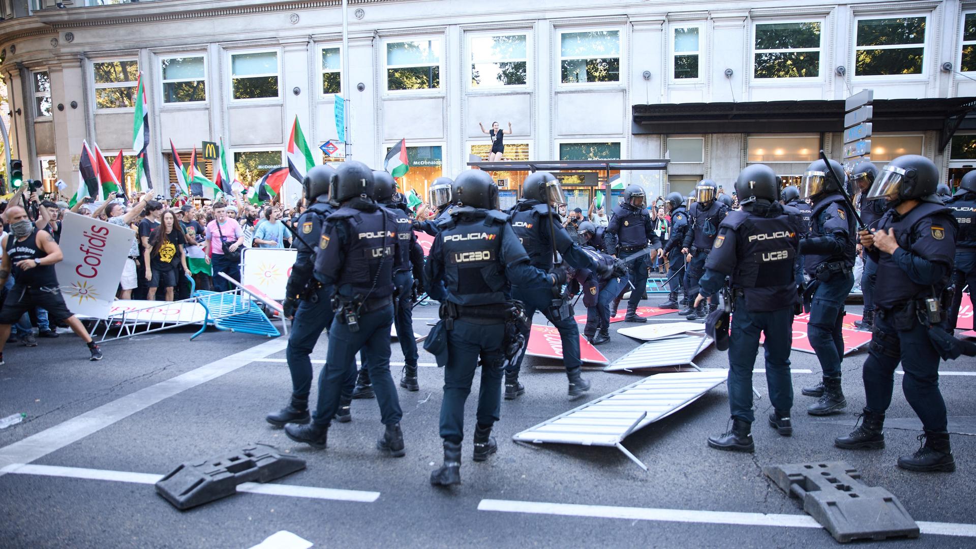 Polizisten in Einsatzkleidung steigen über umgestoßene Absperrgitter hinweg zu Demonstranten, die Palästina-Flaggen schwenken. Polizisten in Einsatzkleidung steigen über umgestoßene Absperrgitter hinweg zu Demonstranten, die Palästina-Flaggen schwenken.