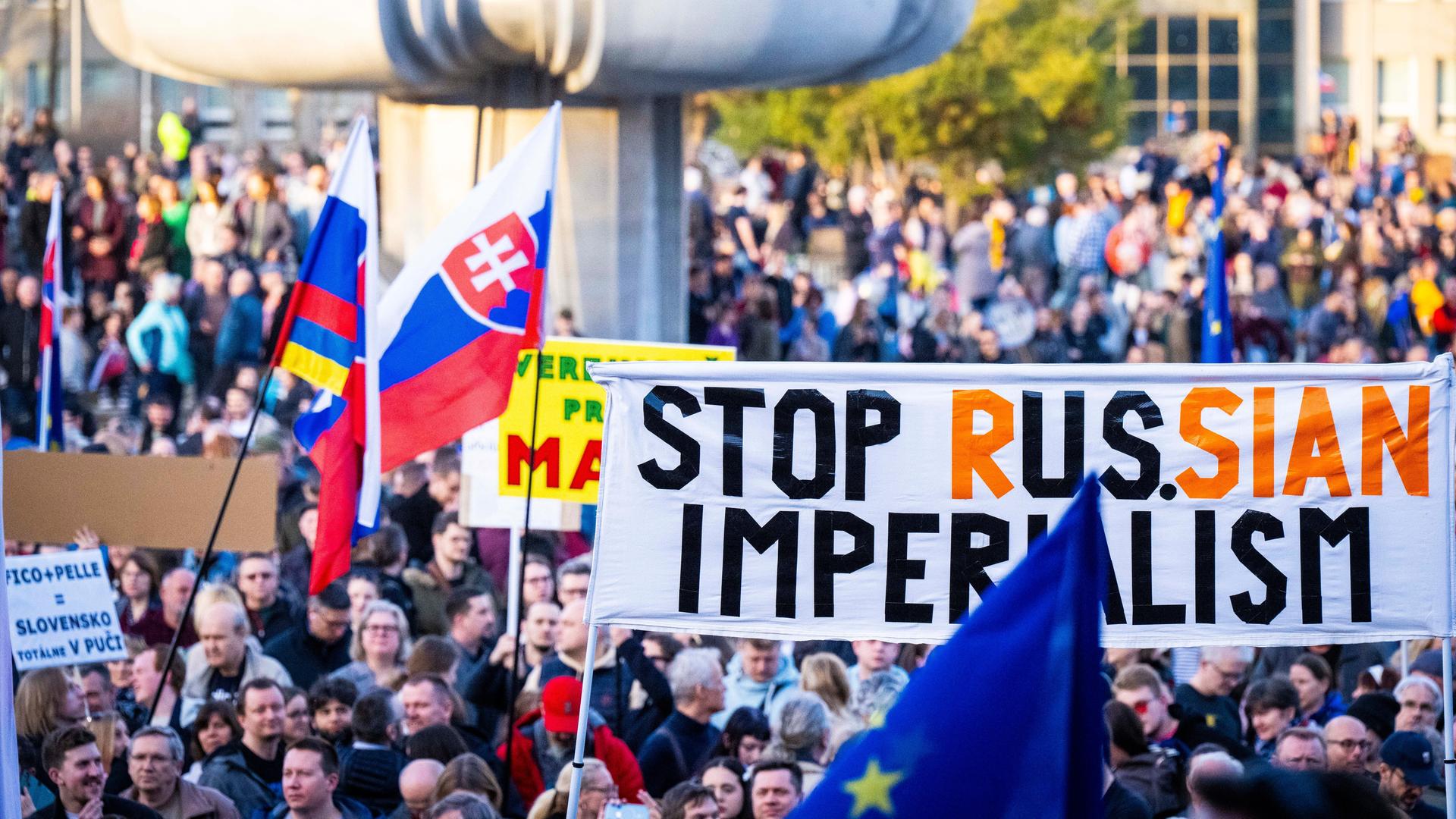 Viele Menschen nehmen auf einem öffentlichen Plant an einer Demonstration teil. Sie schwenken Fahnen und halten Protestbanner.