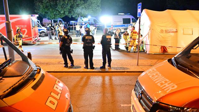 Polizei-Autos und Polizisten stehen auf einer Straße. Es ist Nacht.