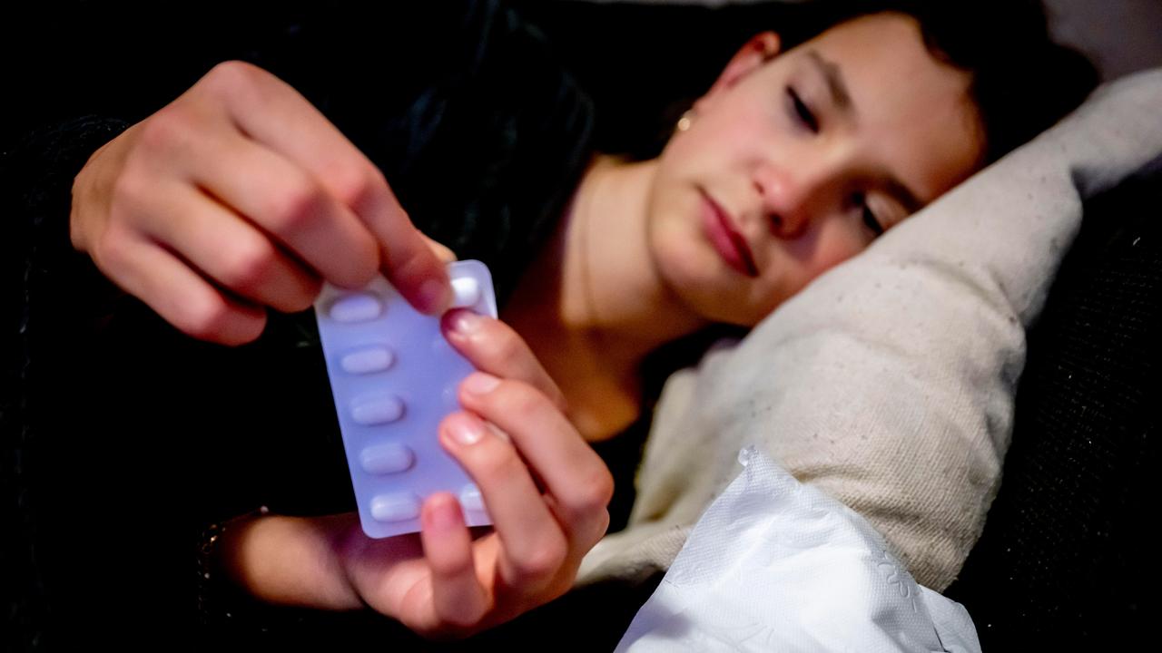 Eine junge Frau liegt im Bett und drückt eine Tablette aus einer Sichtverpackung.
