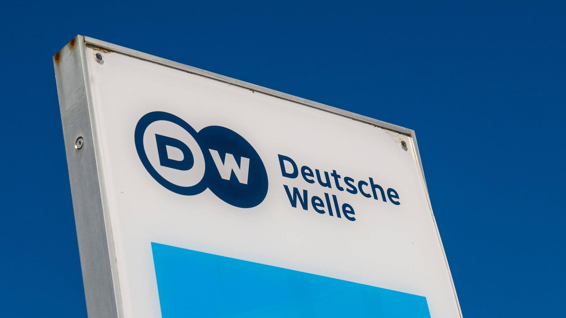 Das Logo der Deutschen Welle auf einem Schild unter dunkelblauem Himmel.