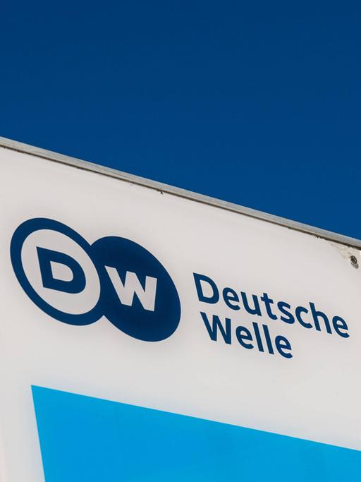Das Logo der Deutschen Welle auf einem Schild, dahinter blauer Himmel.