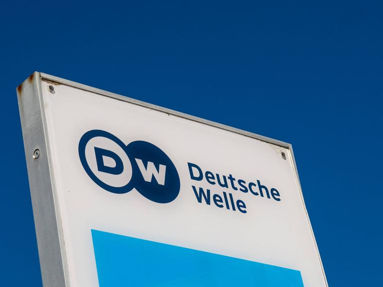 Das Logo der Deutschen Welle auf einem Schild, dahinter blauer Himmel.