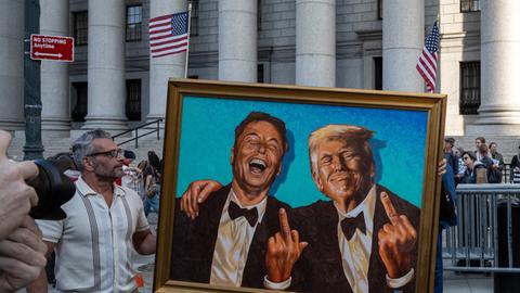 Inmitten von Demonstranten, die am Foley Square in New York gegen die Politik von Donald Trump in Bezug auf Zölle, Arbeitnehmerrechte und Bürgerrechte protestieren, ist ein Gemälde oder Kunstwerk mit den Figuren von Elon Musk und Trump zu sehen. 
