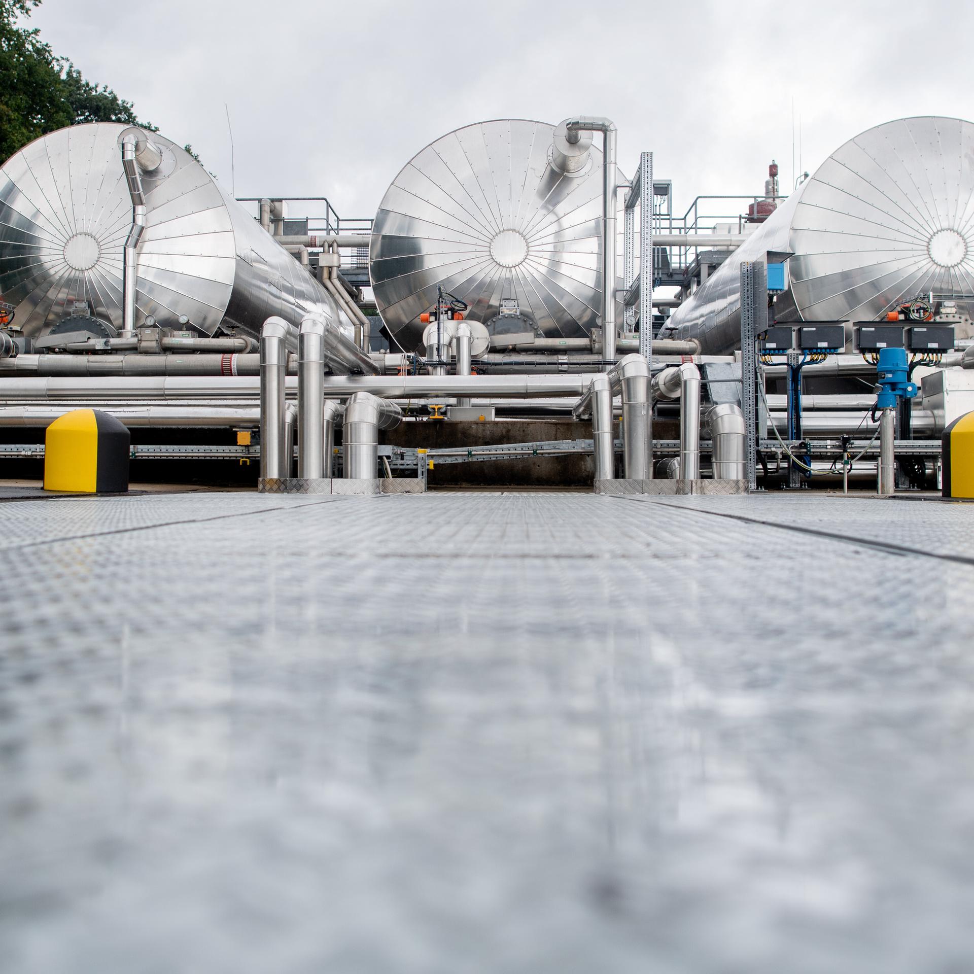 Der Blick geht direkt auf drei silberne Prozesswassertanks einer technische Anlagen zur Ein- und Ausspeicherung von Erdgas auf dem Gelände des Erdgasspeichers Rehden der SEFE Storage GmbH.