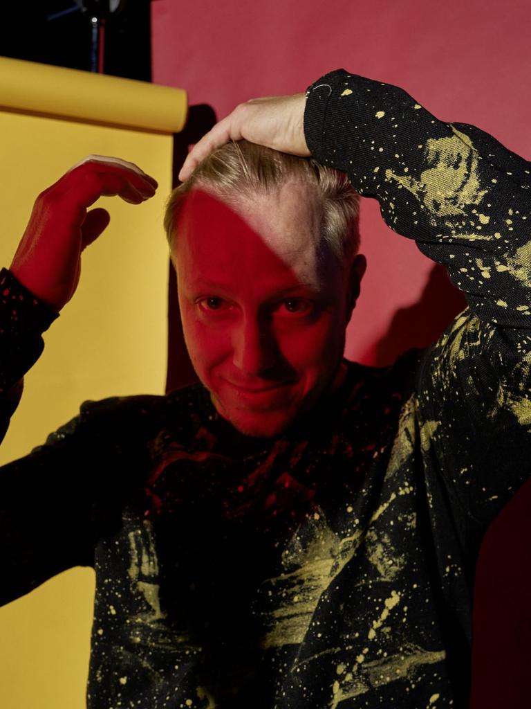 Ein buntes Portrait vor Papierbahnen in rot, gelb und blau. Der Musiker Martin Tingvall streicht sich die blonden Haare zurück, er trägt einen schwarzen Pullover mit wildem, gelbem Muster. Er ist halb im Schatten.