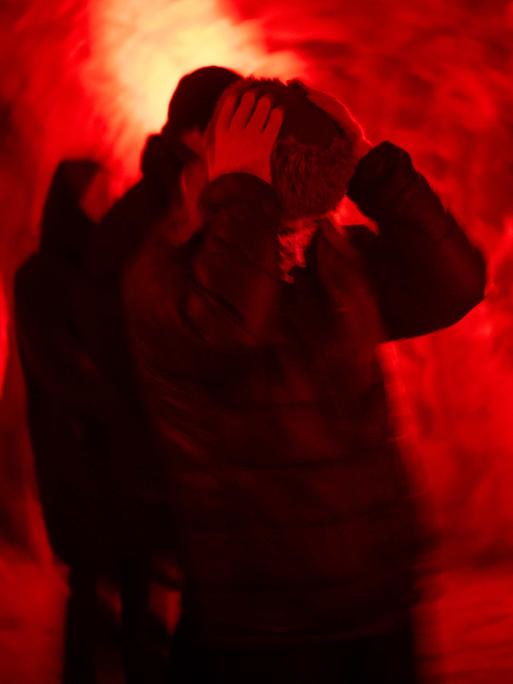 Eine Frau hält sich die Ohren zu, im Hintergrund roter Nebel. Aufgenommen beim Kunstfestival Barents Spektakel in Kirkenes, Norwegen.