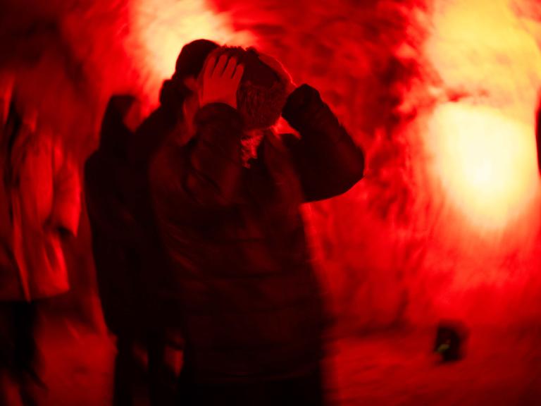 Eine Frau hält sich die Ohren zu, im Hintergrund roter Nebel. Aufgenommen beim Kunstfestival Barents Spektakel in Kirkenes, Norwegen.
