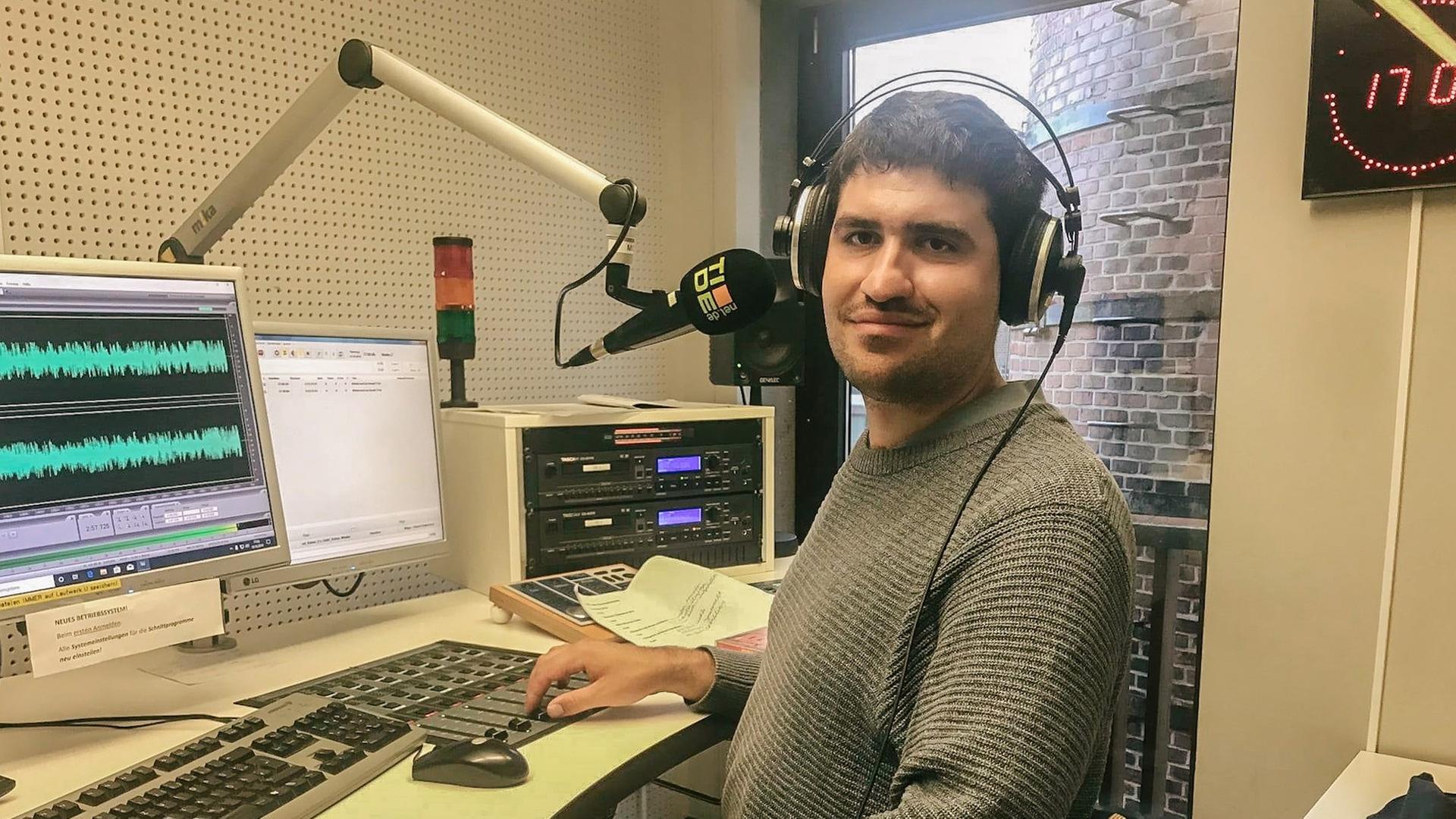 Ein junger Mann mit Kopfhörern auf dem Kopf in einem Radiostudio vor dem Computer