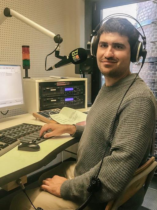 Ein junger Mann mit Kopfhörern auf dem Kopf in einem Radiostudio vor dem Computer