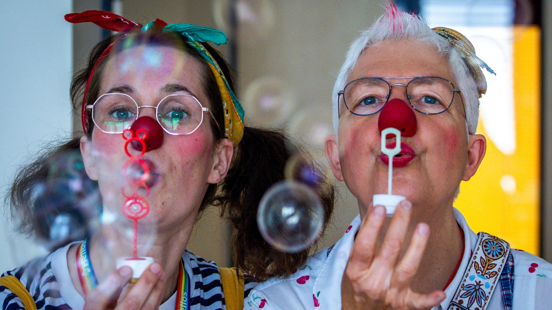 Zwei Frauen, verkleidet als Clowns, machen Seifenblasen.