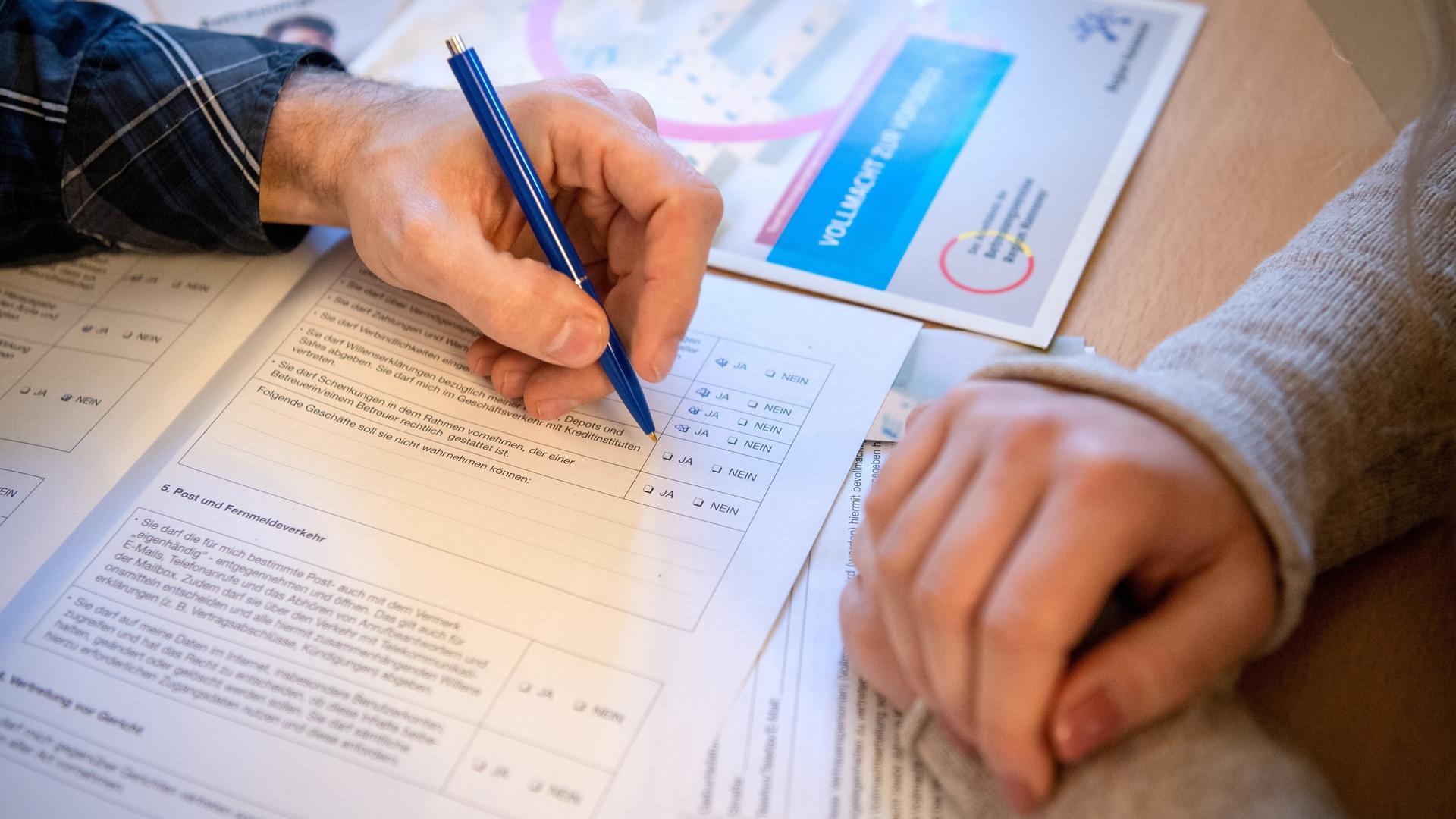 Zwei Personen beugen sich über ein Formular. Eine Person hält in der Hand einen Stift und füllt das Formular aus. Zwei Personen beugen sich über ein Formular. Eine Person hält in der Hand einen Stift und füllt das Formular aus.