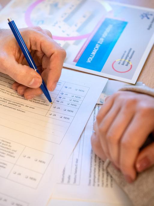 Zwei Personen beugen sich über ein Formular. Eine Person hält in der Hand einen Stift und füllt das Formular aus.
