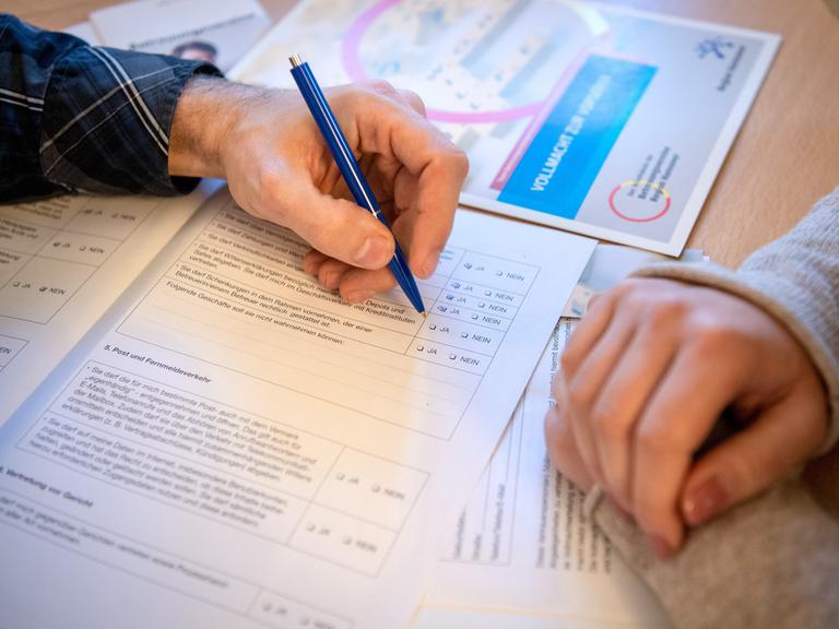 Zwei Personen beugen sich über ein Formular. Eine Person hält in der Hand einen Stift und füllt das Formular aus.