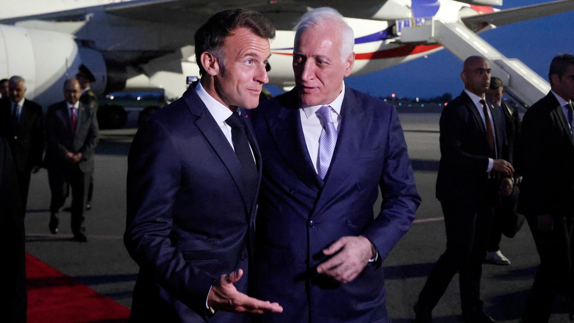 Frankreichs Präsident Emmanuel Macron an der Seite des armenischen Präsidenten Vahagn Khachaturyan. Im Hintergrund ein Flugzeug.