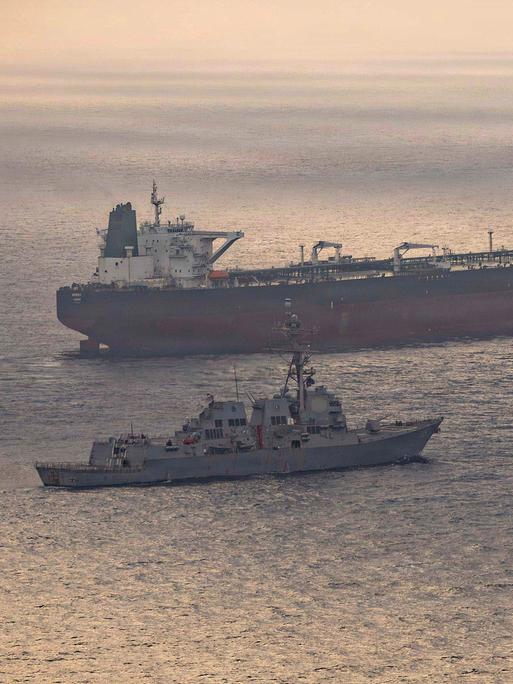 Ein US-Kriegsschiff und ein iranischer Tanker Anfang Mai in der Straße von Hormus. Auf dem Wasser spiegelt sich die untergehende Sonne.