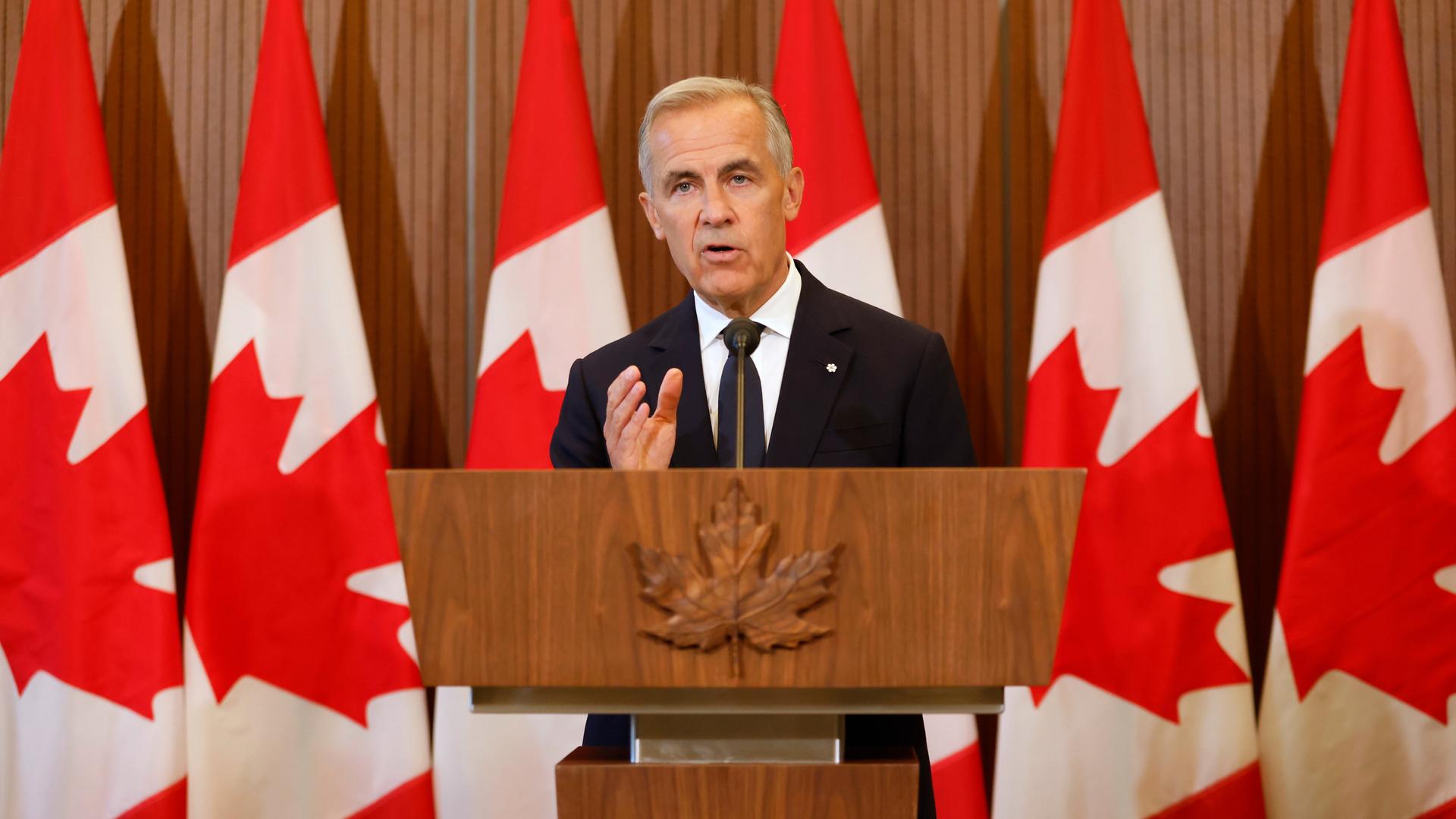 Kanadas Premierminister Mark Carney spricht an einem Rednerpult und vor kanadischen Flaggen auf einer Pressekonferenz.