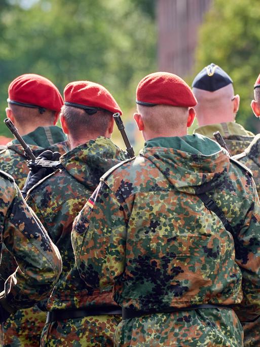 Eine Gruppe von Soldaten der Deutschen Bundeswehr in Tarnuniformen stehen in Formation mit Gewehr bewaffnet bei einem Appell.