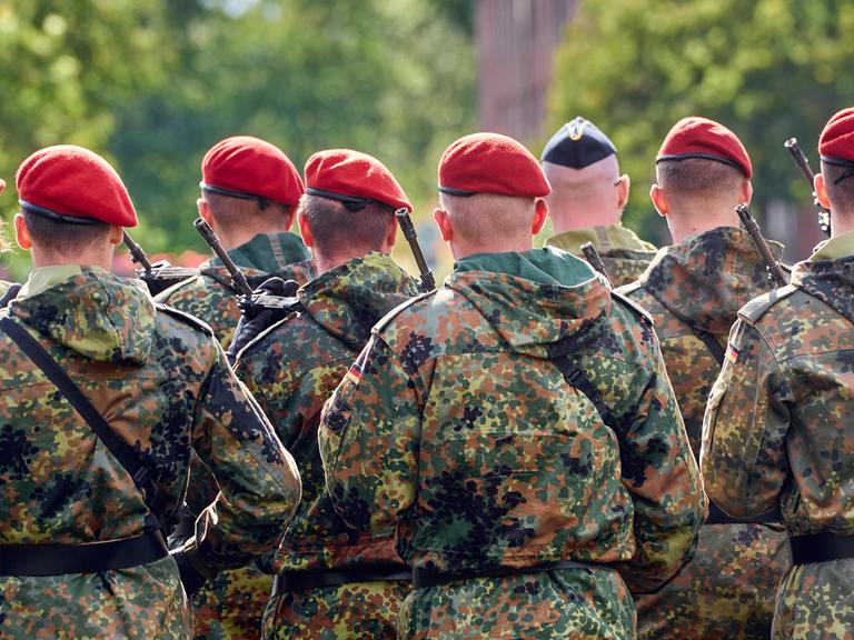 Eine Gruppe von Soldaten der Deutschen Bundeswehr in Tarnuniformen stehen in Formation mit Gewehr bewaffnet bei einem Appell.