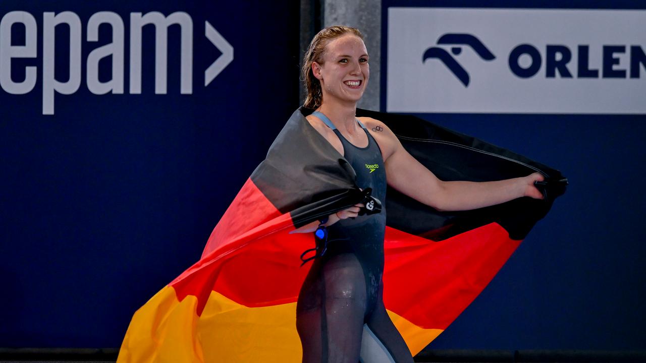 Das Bild zeigt die Sportlerin Isabel Gose im Schwimmanzug. Sie lächelt zufrieden und hält eine Deutschlandflagge quer über die Schultern.