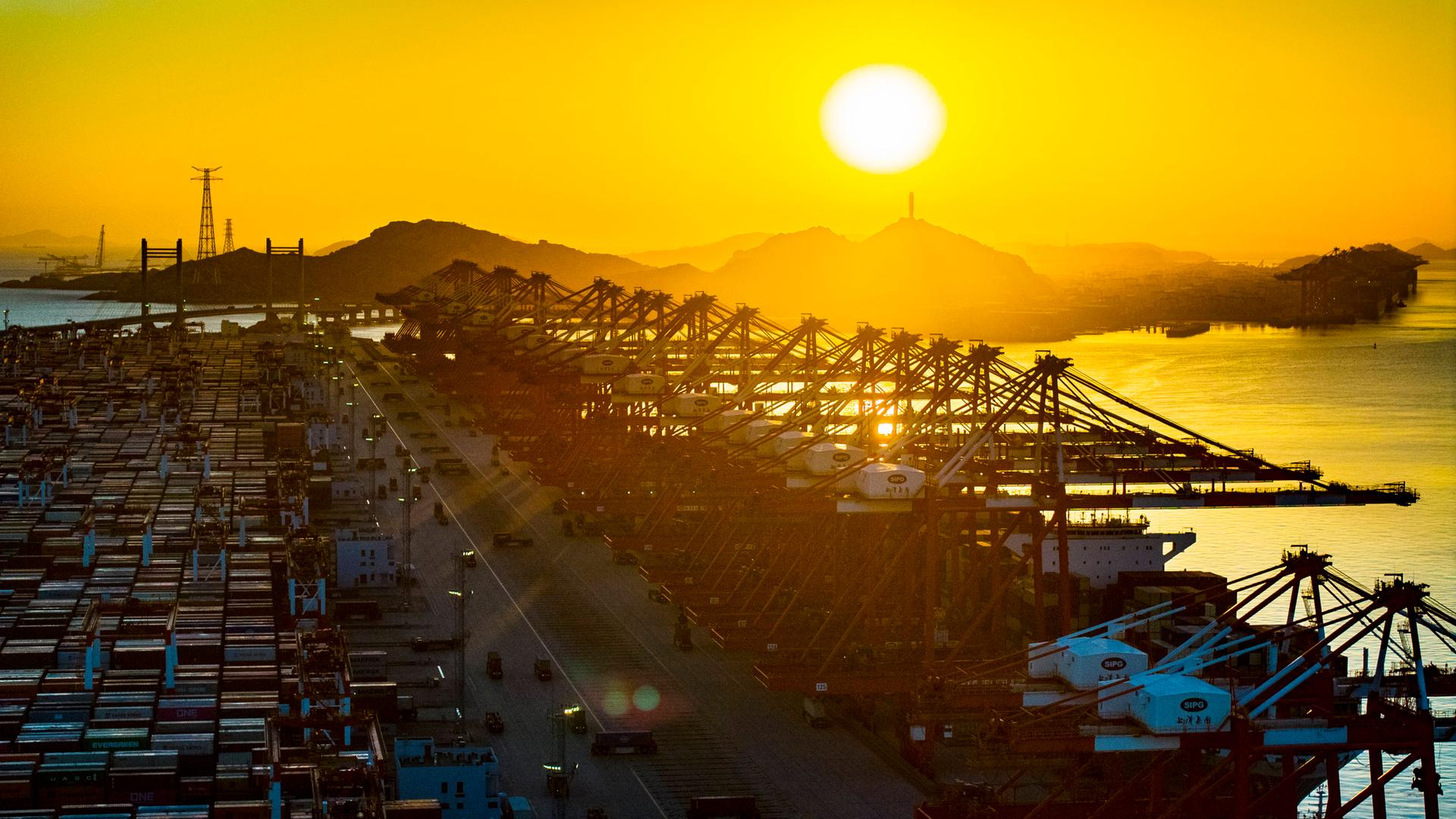 Am Hafen von Shanghai stehen Container und Kräne, während die Sonne aufgeht Am Hafen von Shanghai stehen Container und Kräne, während die Sonne aufgeht