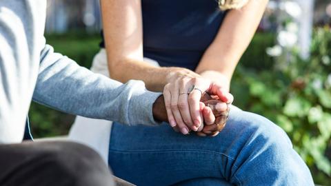 Eine junge Frau hält einer anderen Person zum Trost die Hand