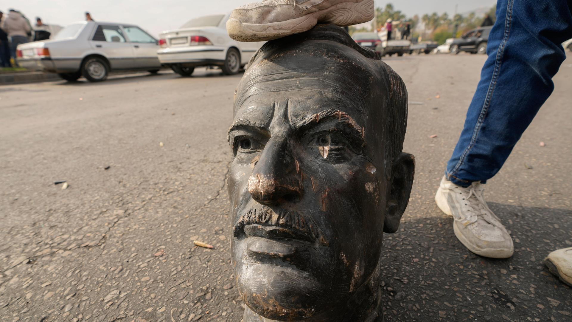 Ein Mann stellt sein Bein auf den Kopf einer zerstörten Assad-Statue auf den Straßen von Damaskus