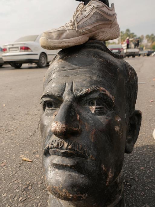 Ein Mann stellt sein Bein auf den Kopf einer zerstörten Assad-Statue auf den Straßen von Damaskus