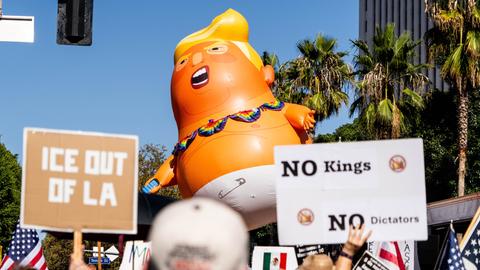Demonstration gegen Donald Trump in Los Angeles mit Plakat "No King ". Außerdem werden noch andere Schilder in die Höhe gehalten sowie eine große Puppe, die Donald Trump darstellen soll.