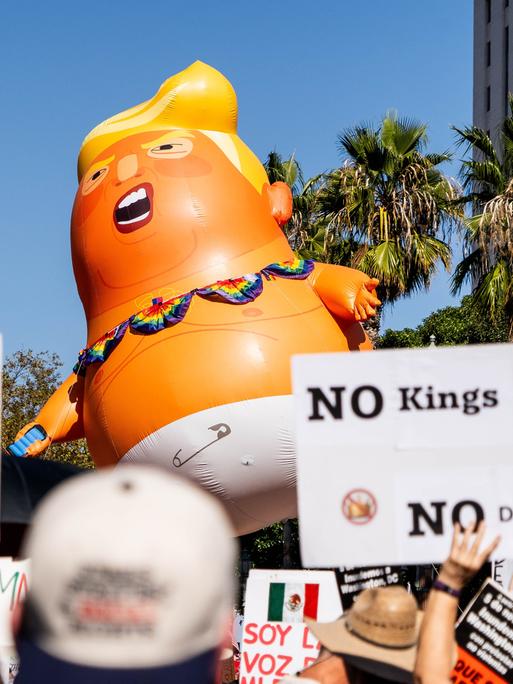 Demonstration gegen Donald Trump in Los Angeles mit Plakat "No King ". Außerdem werden noch andere Schilder in die Höhe gehalten sowie eine große Puppe, die Donald Trump darstellen soll.