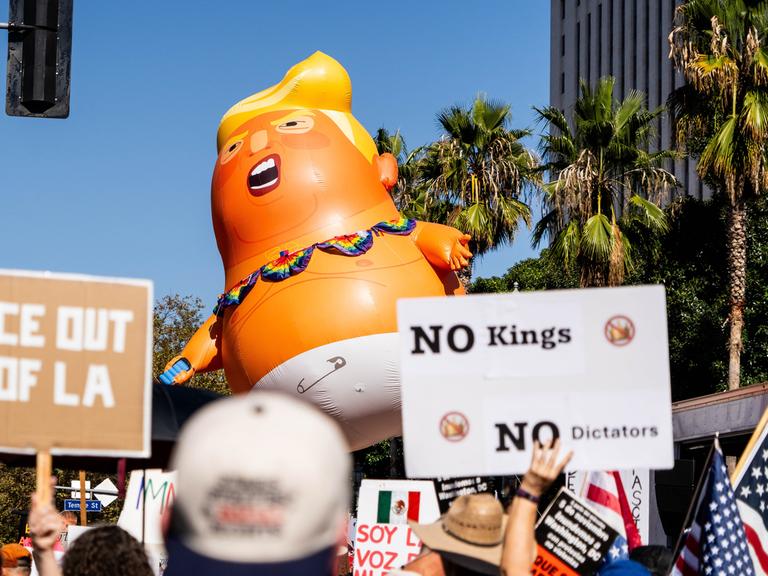 Demonstration gegen Donald Trump in Los Angeles mit Plakat "No King ". Außerdem werden noch andere Schilder in die Höhe gehalten sowie eine große Puppe, die Donald Trump darstellen soll.