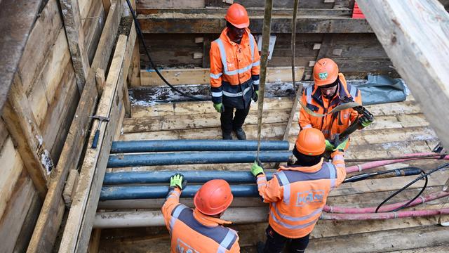 Vier Menschen mit orangefarbenen Helmen und Jacken stehen und arbeiten am 5.1.2026 in einer Baugrube mit Rohren und Kabeln. Vier Menschen mit orangefarbenen Helmen und Jacken stehen und arbeiten am 5.1.2026 in einer Baugrube mit Rohren und Kabeln.
