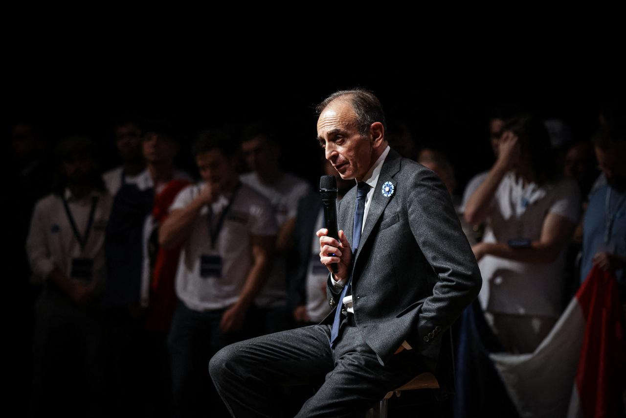 Éric Zemmour sitzt bei einer Wahlkampfveranstaltung auf einem Stuhl und spricht in ein Mikrofon.