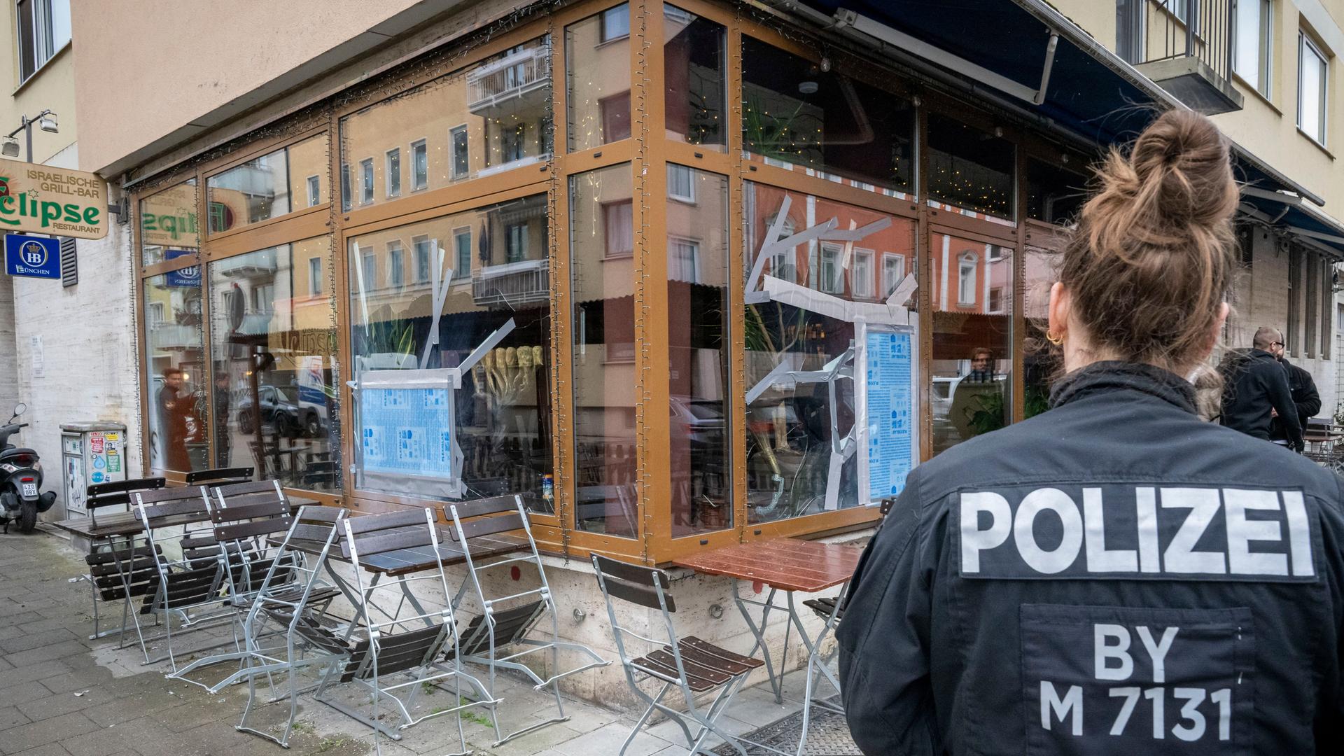 Bayern, München: Eine Polizistin steht vor einem israelischen Restaurant, in dem nach einem Angriff zerbrochene Scheiben notdürftig repariert wurden. 