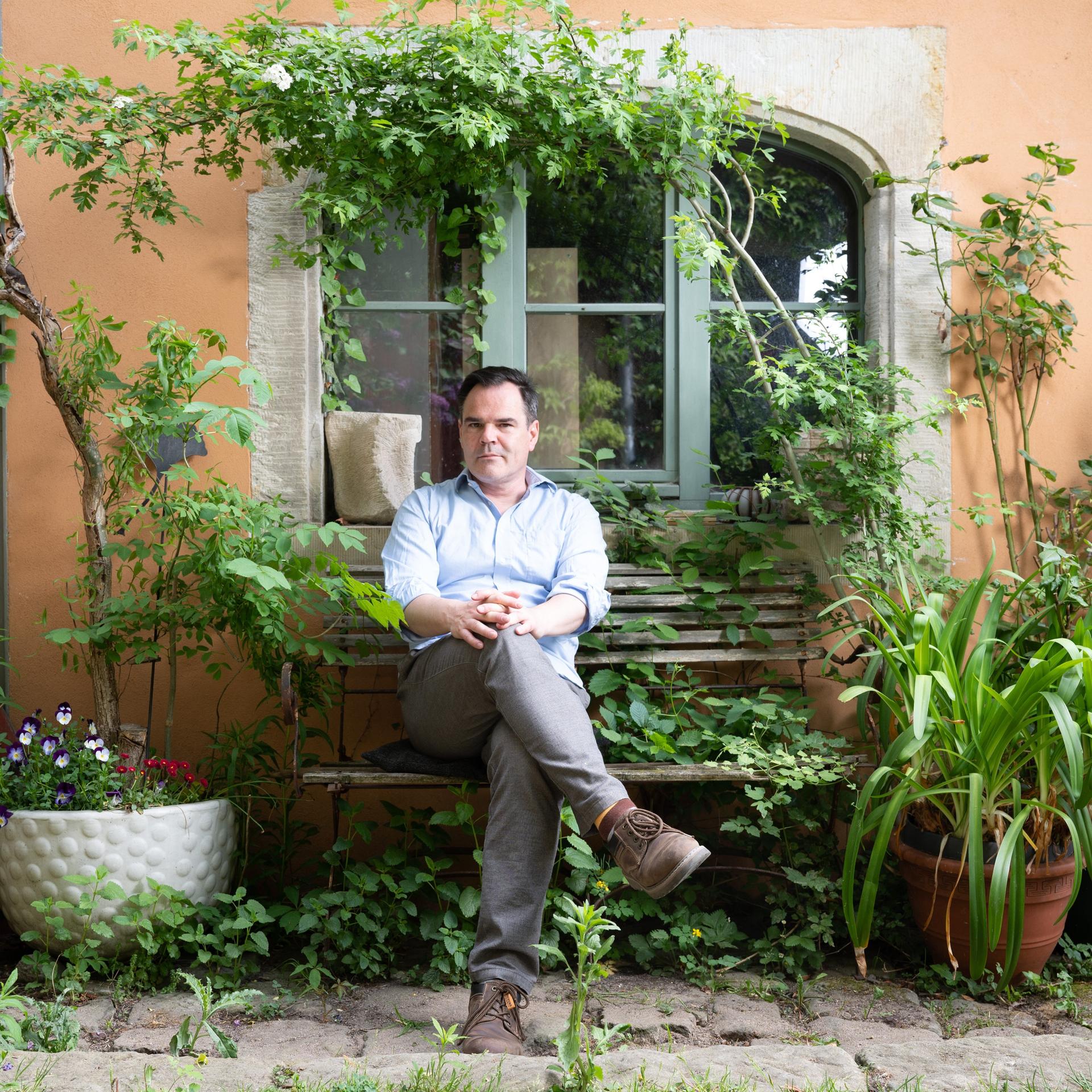 Der Schriftsteller Uwe Tellkamp sitzt inmitten von Pflanzen auf einer Bank.
