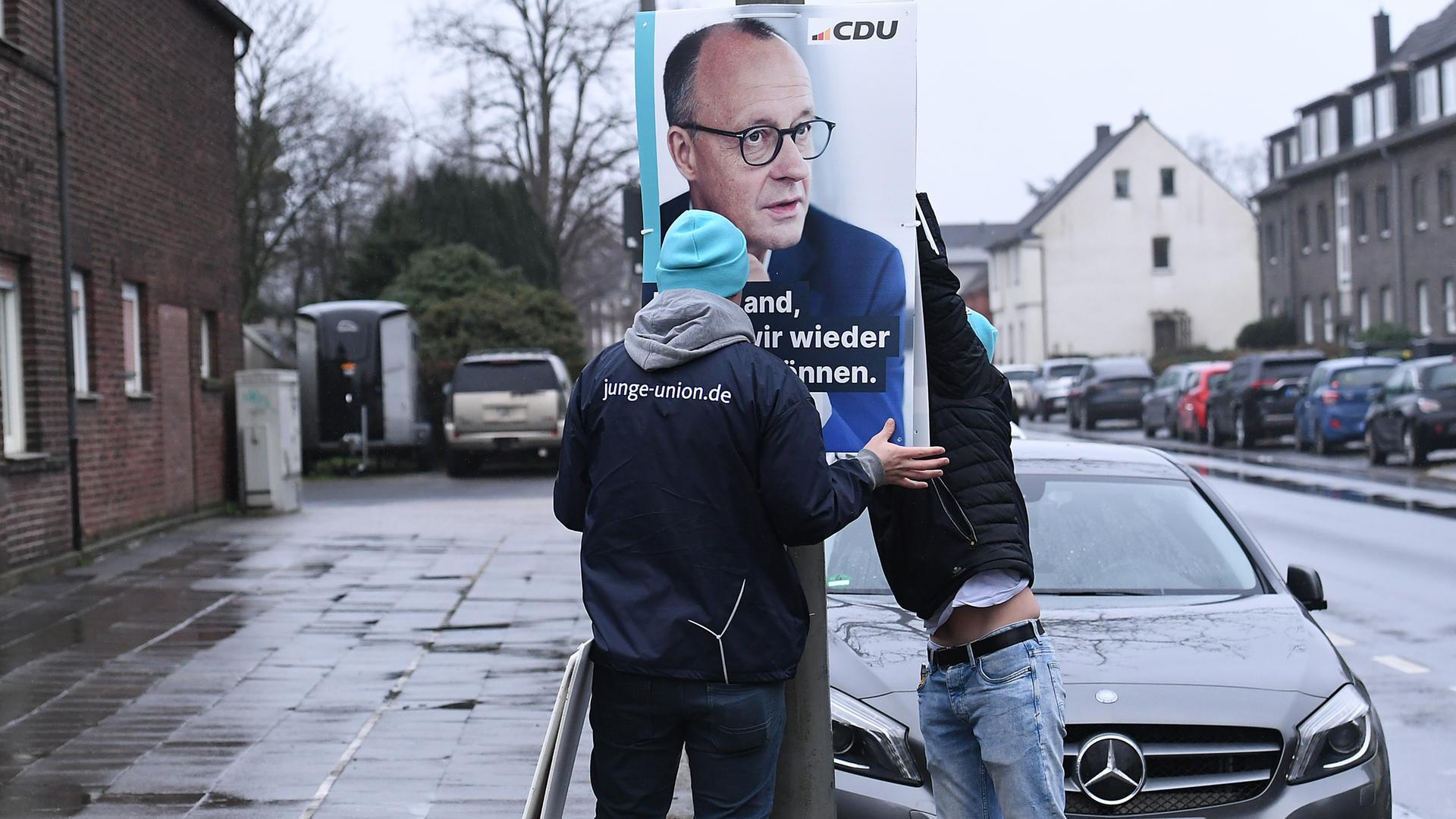 Mitarbeiter der Jungen Union hängen ein Wahlplakat mit dem Spitzenkandidaten der Union, Friedrich Merz, an einem Laternenmast in Oberhausen auf. 