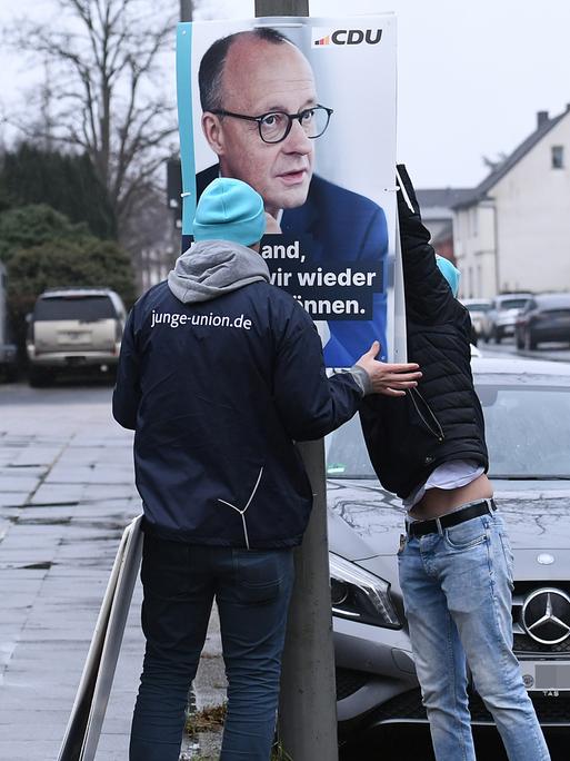 Mitarbeiter der Jungen Union hängen ein Wahlplakat mit dem Spitzenkandidaten der Union, Friedrich Merz, an einem Laternenmast in Oberhausen auf. 