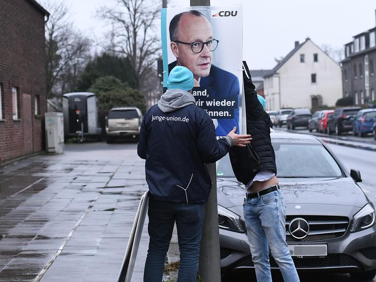 Mitarbeiter der Jungen Union hängen ein Wahlplakat mit dem Spitzenkandidaten der Union, Friedrich Merz, an einem Laternenmast in Oberhausen auf. 